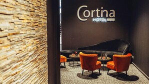 A modern interior with a stone wall, a black leather sofa, and orange chairs. - Cortina Hotel (Wevelgem)