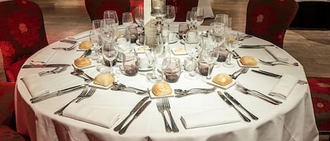 A round dining table set for a meal with multiple wine glasses, plates, and cutlery.