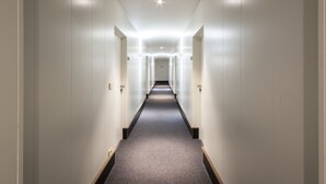 A long, narrow hallway with white walls and a grey carpet. - Cortina Hotel (Wevelgem)