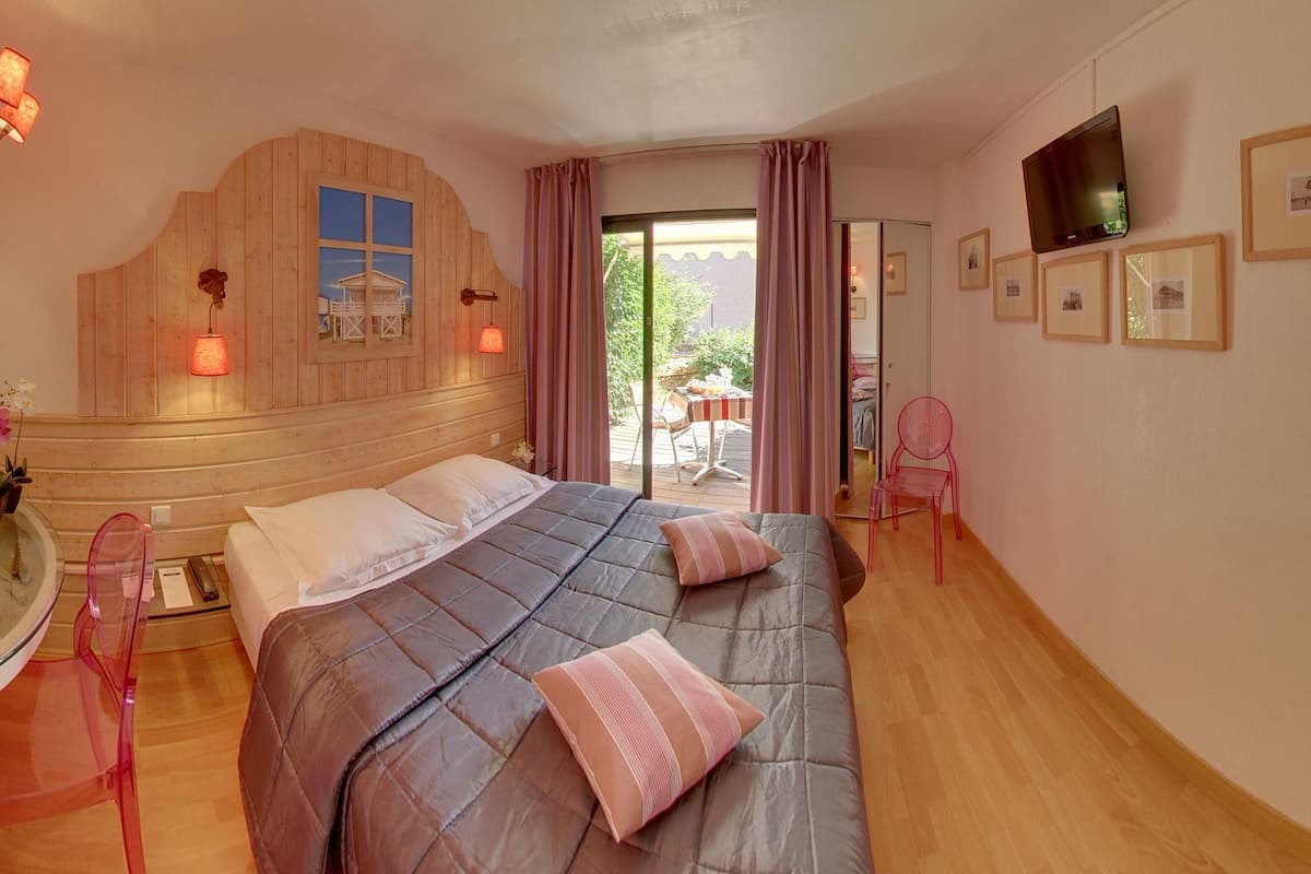 Een slaapkamer met een groot bed, een houten hoofdbord, een glazen tafel met een stoel, en een televisie aan de muur.