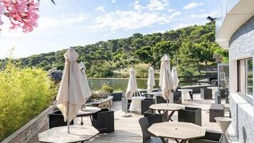 Un patio al aire libre con mesas y sillas, sombrillas y vistas a un lago y árboles.