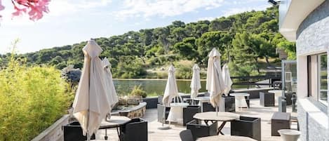 An outdoor patio with tables and chairs, umbrellas, and a view of a lake and trees.