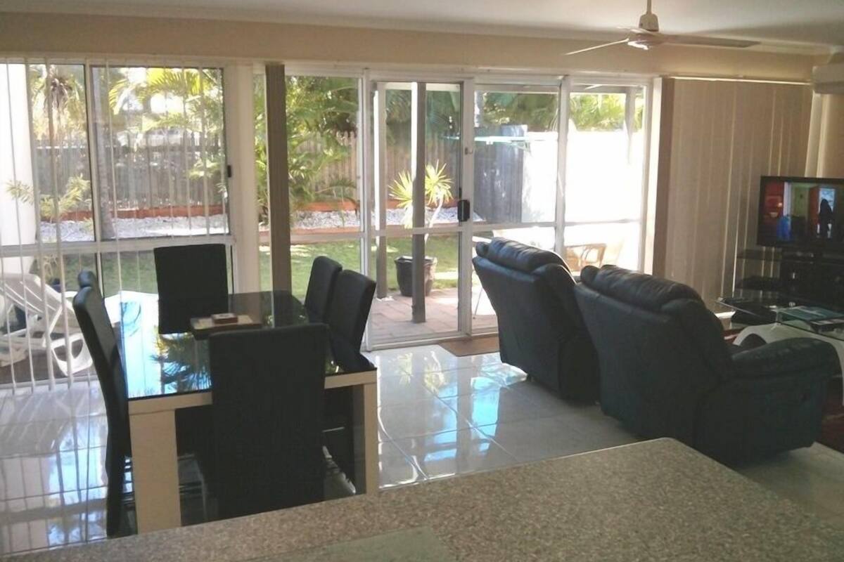 Uma sala de estar ampla, com mesa de jantar de vidro, assentos confortáveis e uma televisão.