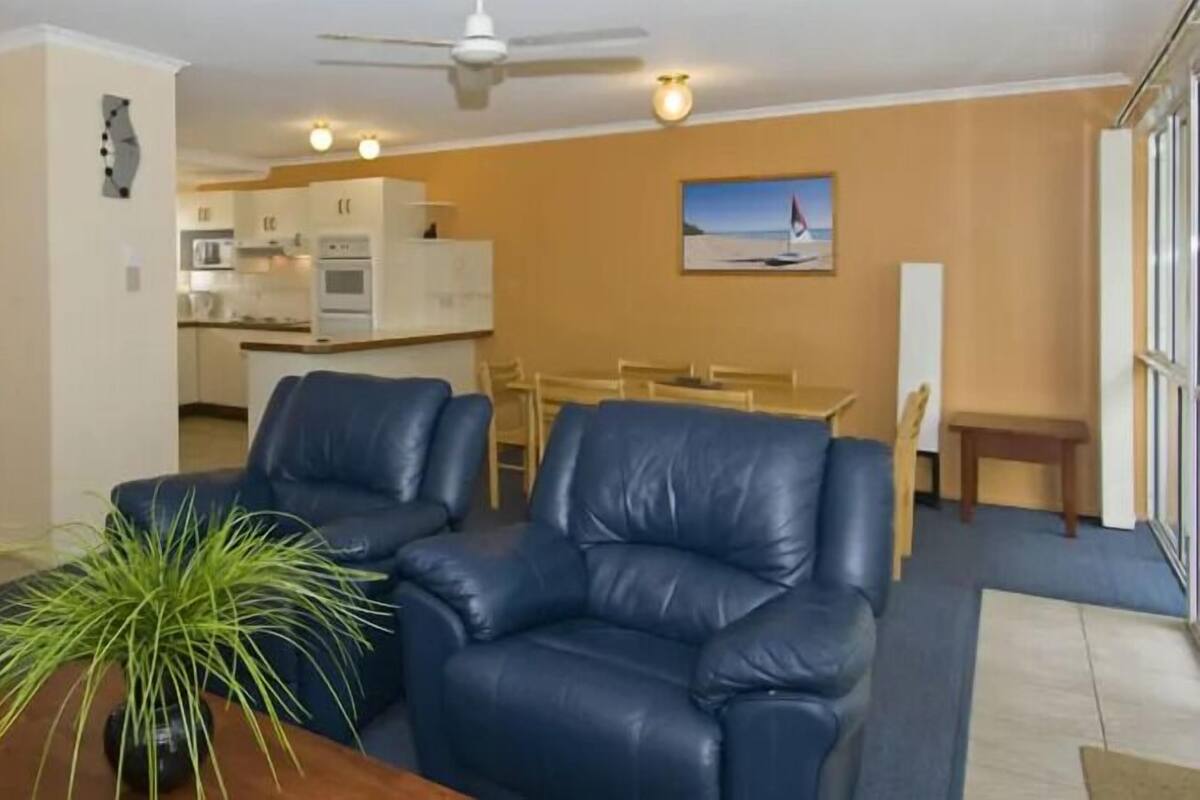 Uma sala de estar com dois sofás de couro azul, uma mesa de centro com uma planta e uma área de jantar com mesa e cadeiras.