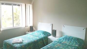Una camera da letto con due letti singoli, un ventilatore a soffitto, una finestra con tende e un comodino con una lampada.