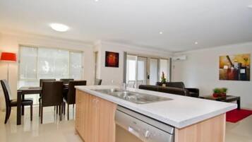 A modern kitchen with a central island, dining area with chairs, and a red rug.