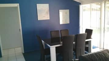 Un comedor con una mesa, sillas, una puerta y un ventanal con persianas.