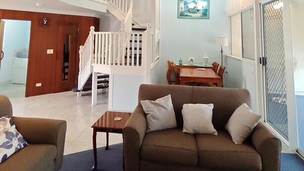 A spacious living room with a high ceiling, a staircase, a dining area, and a view through a glass door. - Bay Hideaway Resort (Eli Waters)