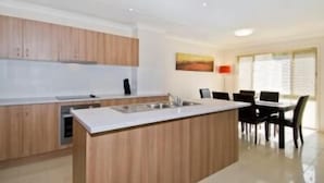 A modern kitchen with wooden cabinets, a central island, and a dining area with a table and chairs. - Bay Hideaway Resort (Eli Waters)