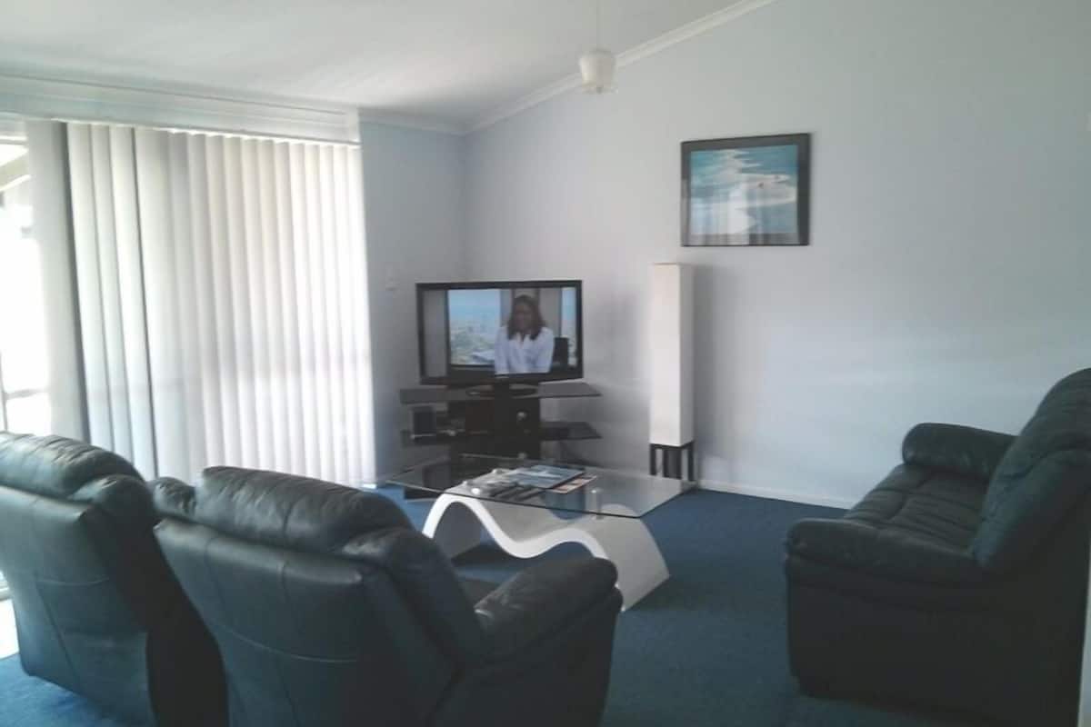 Uma sala de estar com televisão de tela plana, uma mesa de centro de vidro e dois sofás de couro preto.