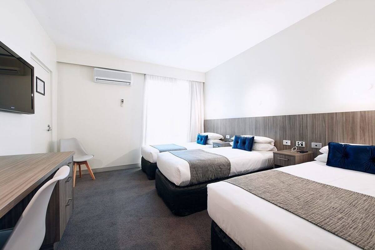A hotel room with two beds, a desk, a chair, an air conditioning unit, and a television.