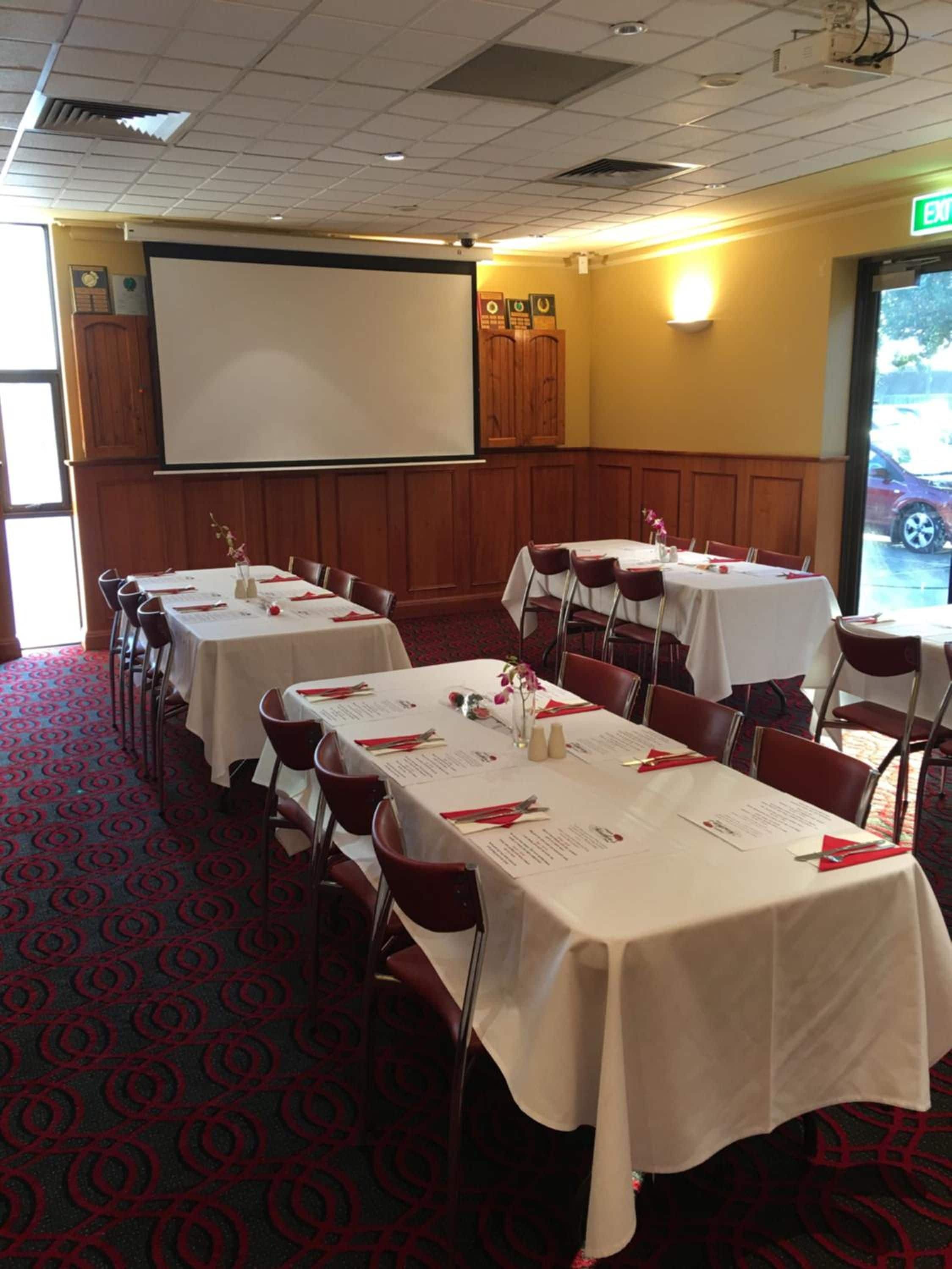 Una sala de conferències amb diverses taules preparades per a dinar, una pantalla de projector i una porta amb un senyal de sortida.