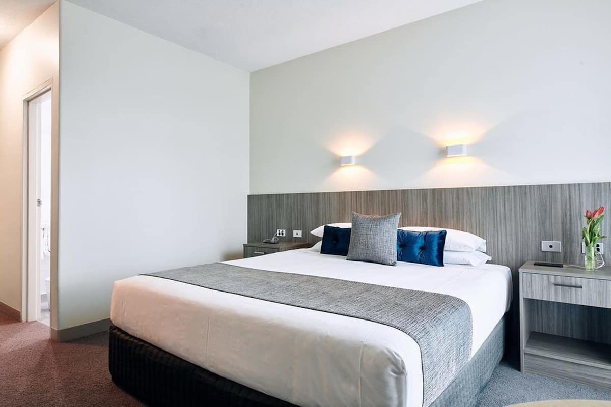 A hotel room with a large bed, two bedside tables, a nightstand, and a wall-mounted light fixture.