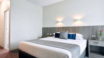 A hotel room with a large bed, two bedside tables, a nightstand, and a wall-mounted light fixture.