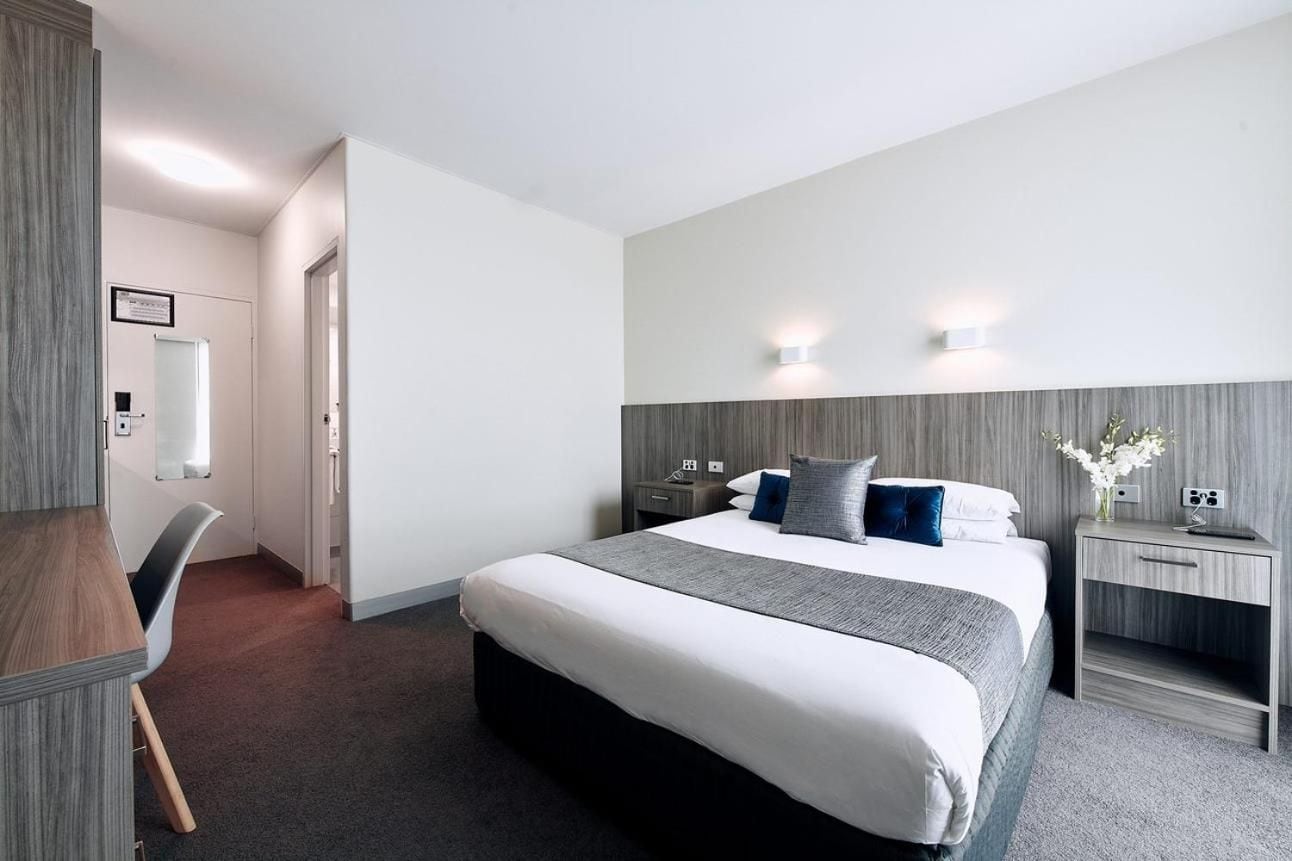 A hotel room with a large bed, bedside tables, a desk, and a chair.