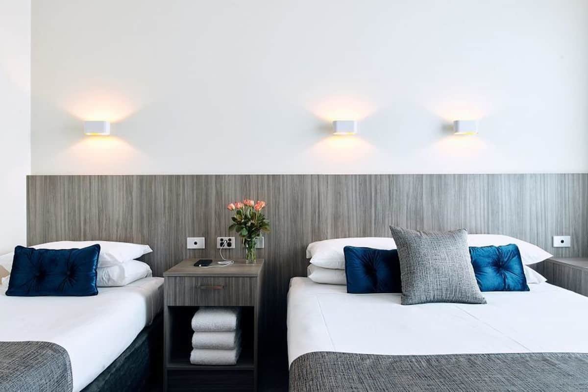 A hotel room with two beds, each with a pillow and a bedside table with a lamp.