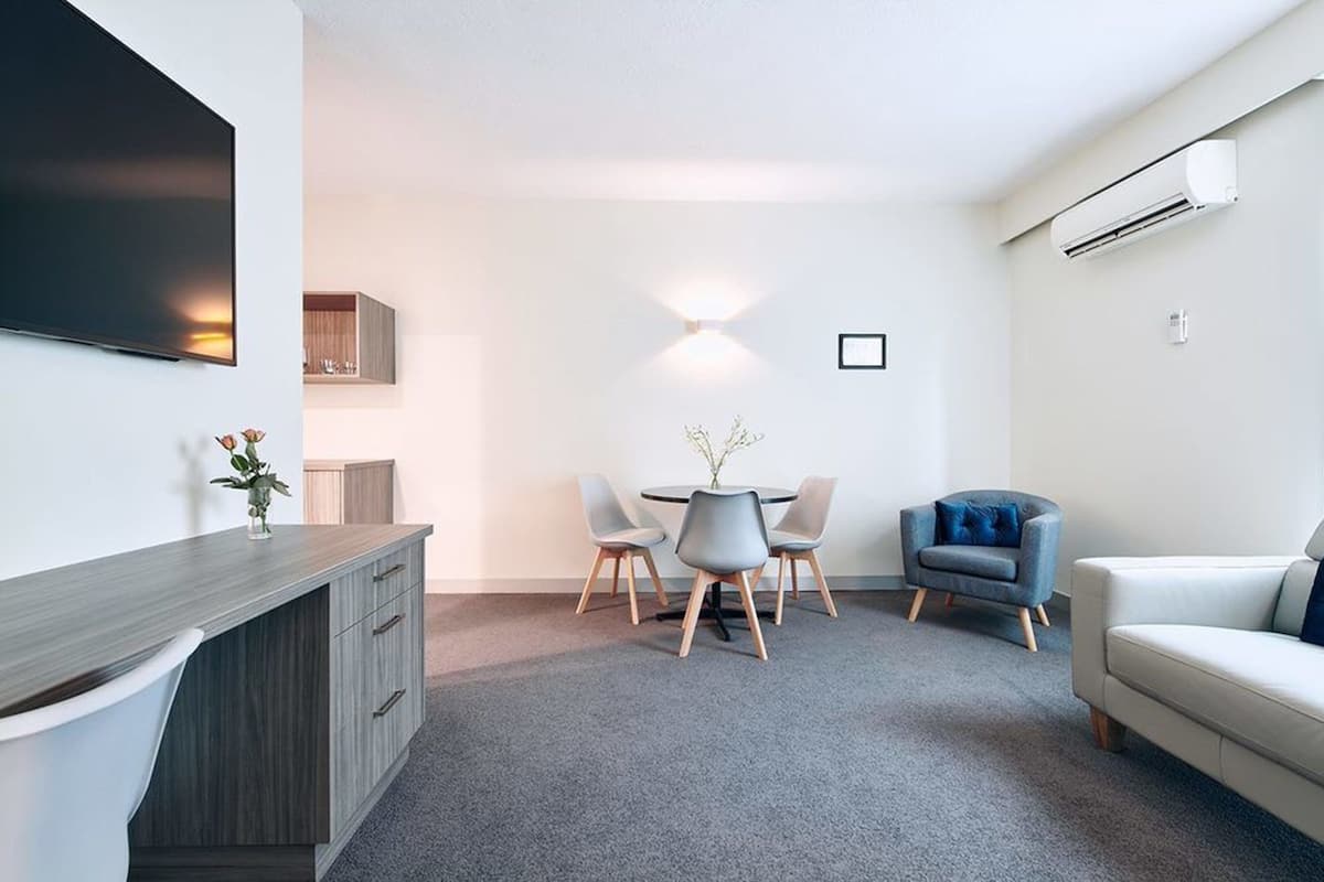 A modern living room with a flat-screen TV, a dining table with chairs, a gray sofa, and an air conditioning unit.