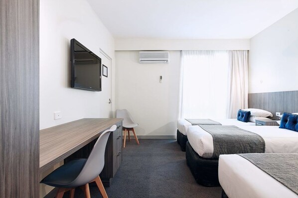 Une chambre d’hôtel équipée d’un bureau, de deux lits, d’une télévision et d’un appareil de climatisation.