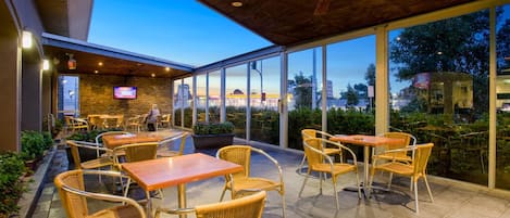 Un espace extérieur aménagé en terrasse, avec des tables et des chaises, un ventilateur de plafond et un écran de télévision.