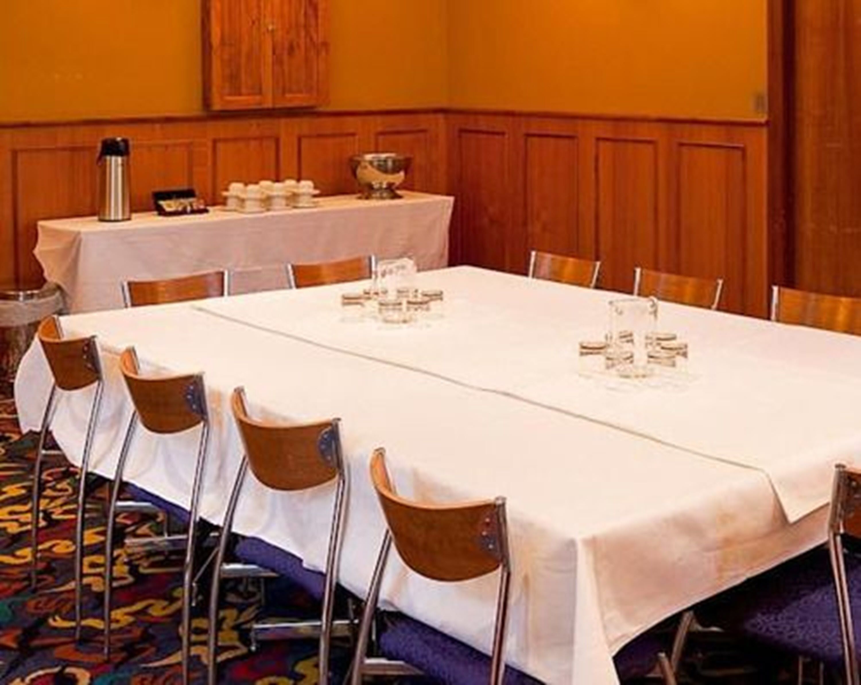 A conference room with a long table set for a meeting, equipped with chairs, a water dispenser, and a coffee pot.