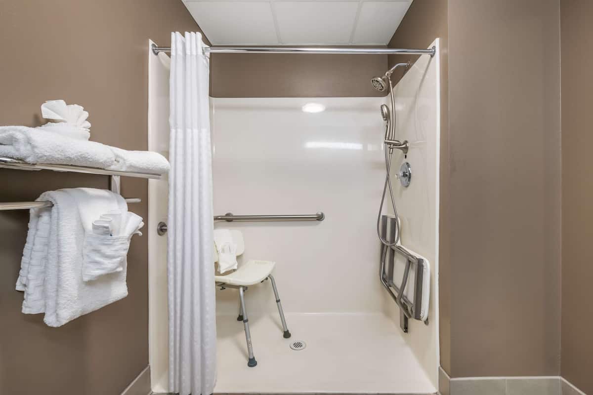Une salle de bain avec une douche, une chaise blanche et un porte-serviettes avec des serviettes.