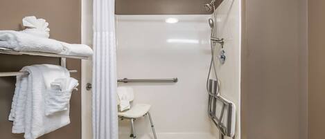 A bathroom with a shower, a white chair, and a towel rack with towels.