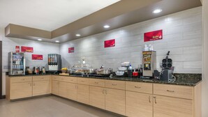 Una cocina moderna con armarios de madera clara, encimeras de granito y electrodomésticos de acero inoxidable. Hay carteles en la pared que publicitan diferentes marcas de café.