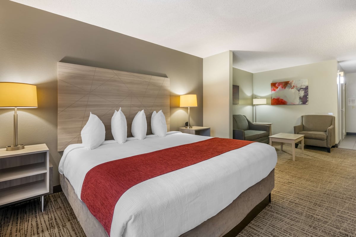 Une chambre d’hôtel avec un grand lit, deux tables de chevet avec des lampes, une chaise, une petite table et un tableau au mur.