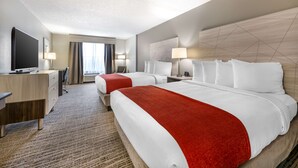 Habitación de hotel con dos camas, un escritorio, un televisor y un ventanal con cortinas.