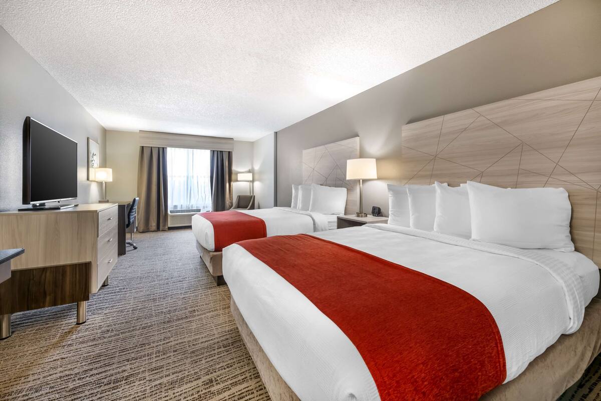 Une chambre d’hôtel avec deux lits, un bureau, une télévision et une grande fenêtre avec des rideaux.