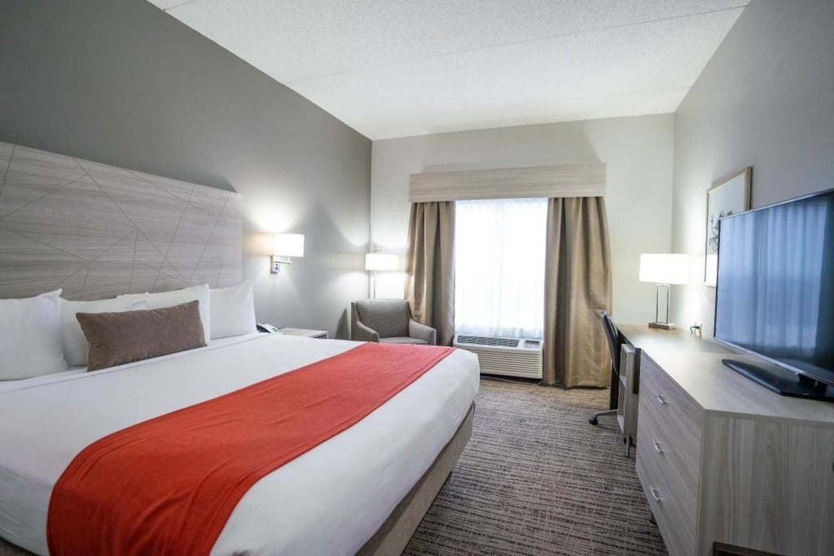 A hotel room with a large bed, a desk, a television, and a window with curtains.
