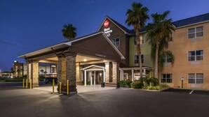 Entrada de hotel con galería techada, palmeras y cielo despejado.