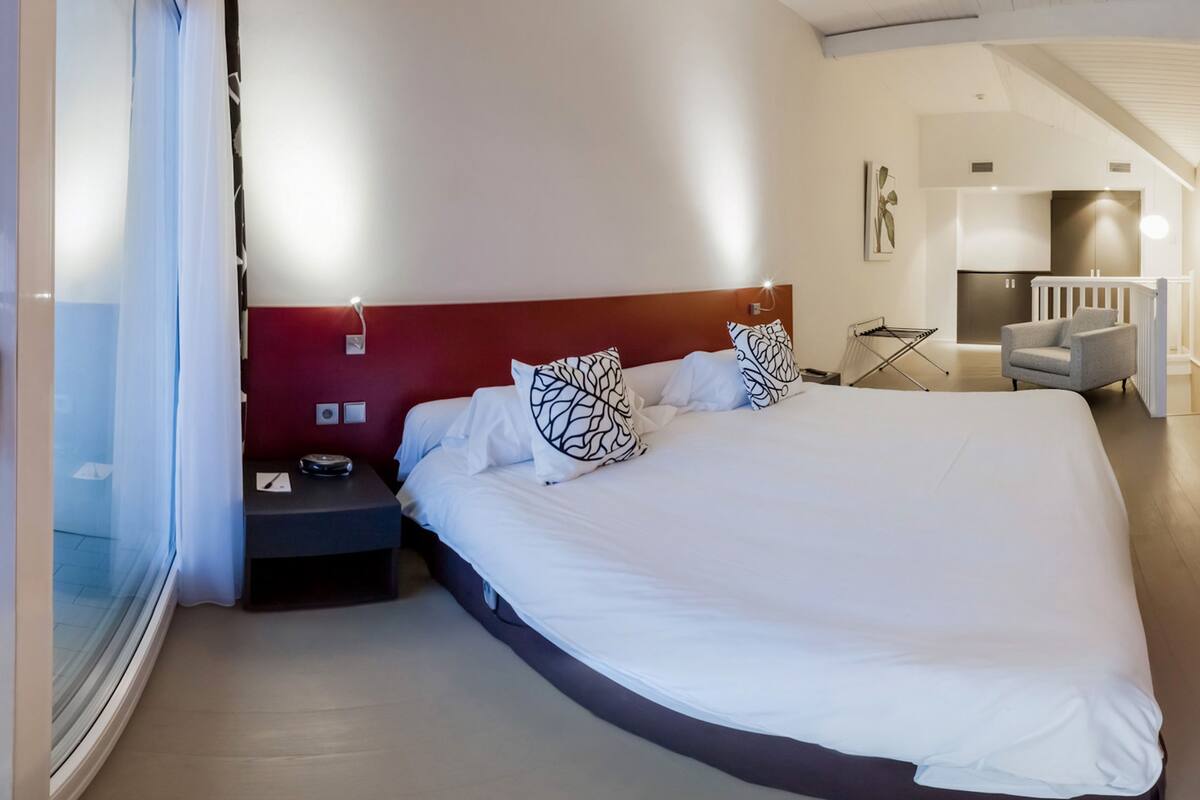 Une chambre d’hôtel moderne avec un grand lit, une table de chevet, une chaise et une vue sur la cuisine.