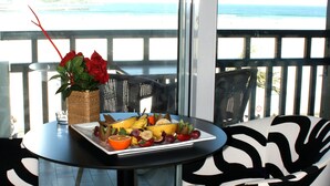 Ein Balkon mit Tisch, gedeckt mit Früchten und einer Blumenvase, mit Blick auf das Meer.