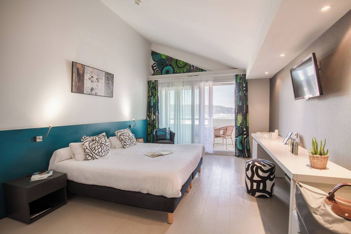 Une chambre d’hôtel moderne équipée d’un lit, d’une table de chevet, d’une télévision et d’un balcon avec vue.