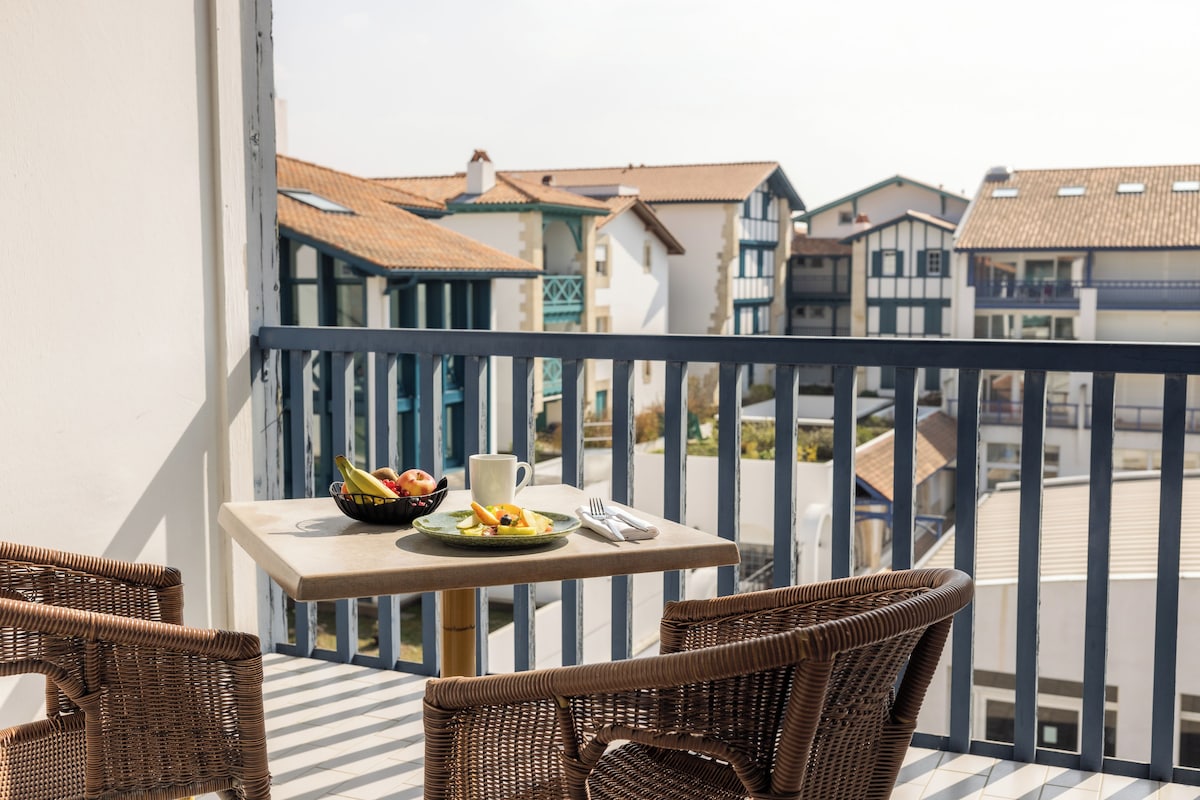 Ein Balkon mit Korbstühlen, einem Tisch mit Obstschale, einer Tasse und einem Teller mit Essen.