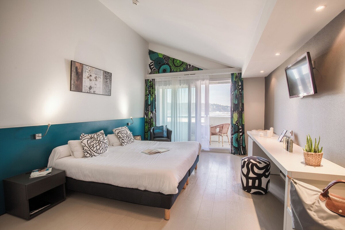 Ein modernes Hotelzimmer mit Bett, Nachttisch, Fernseher und einem Balkon mit Blick.