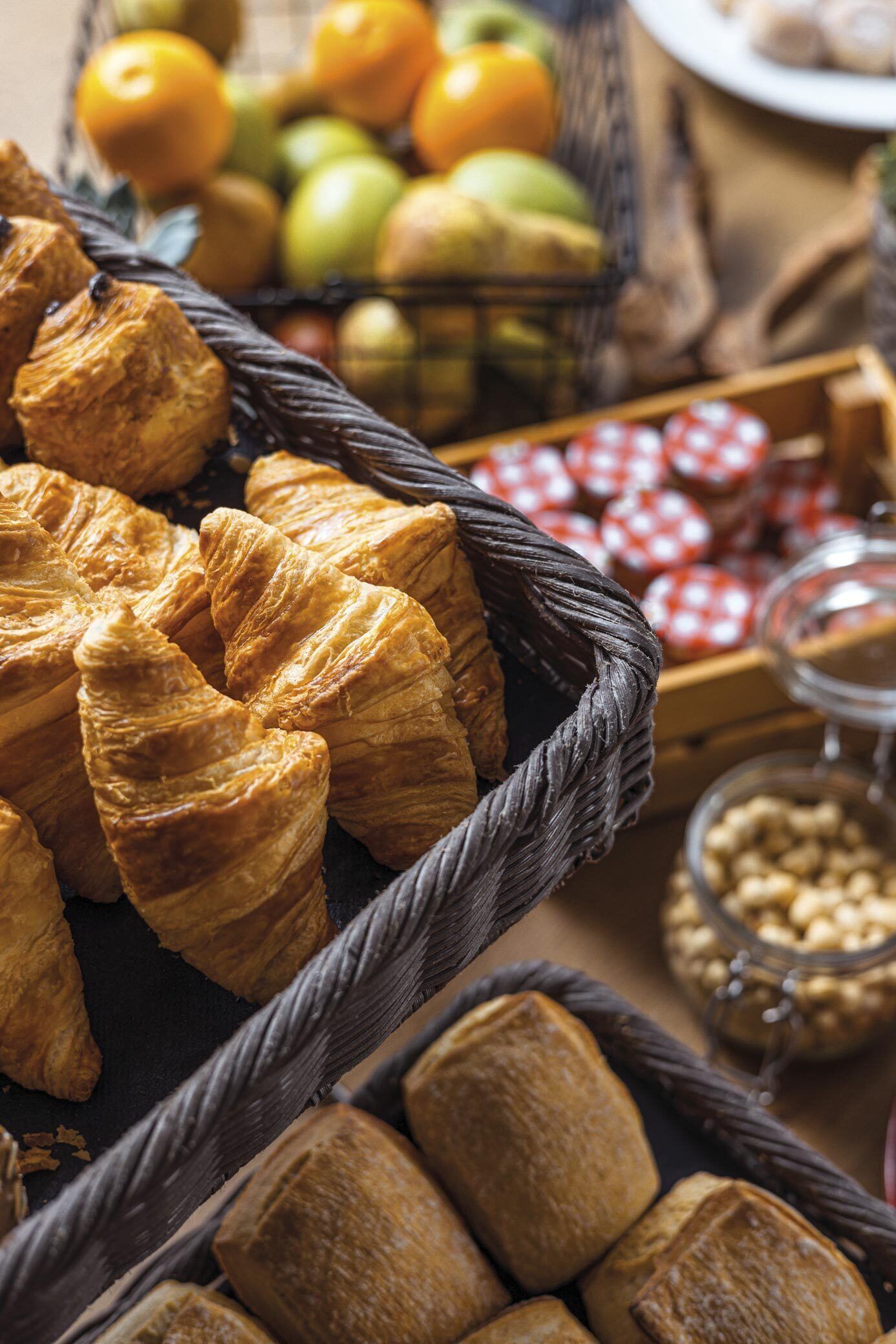 Diversitat de pa i pastissos, com ara croissants, disposats sobre una taula amb cistells i pots de fruits secs.