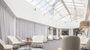 Ein geräumiger, moderner Lounge-Bereich mit weißen Ledersesseln, runden Tischen und einer hohen Decke mit Oberlichter.