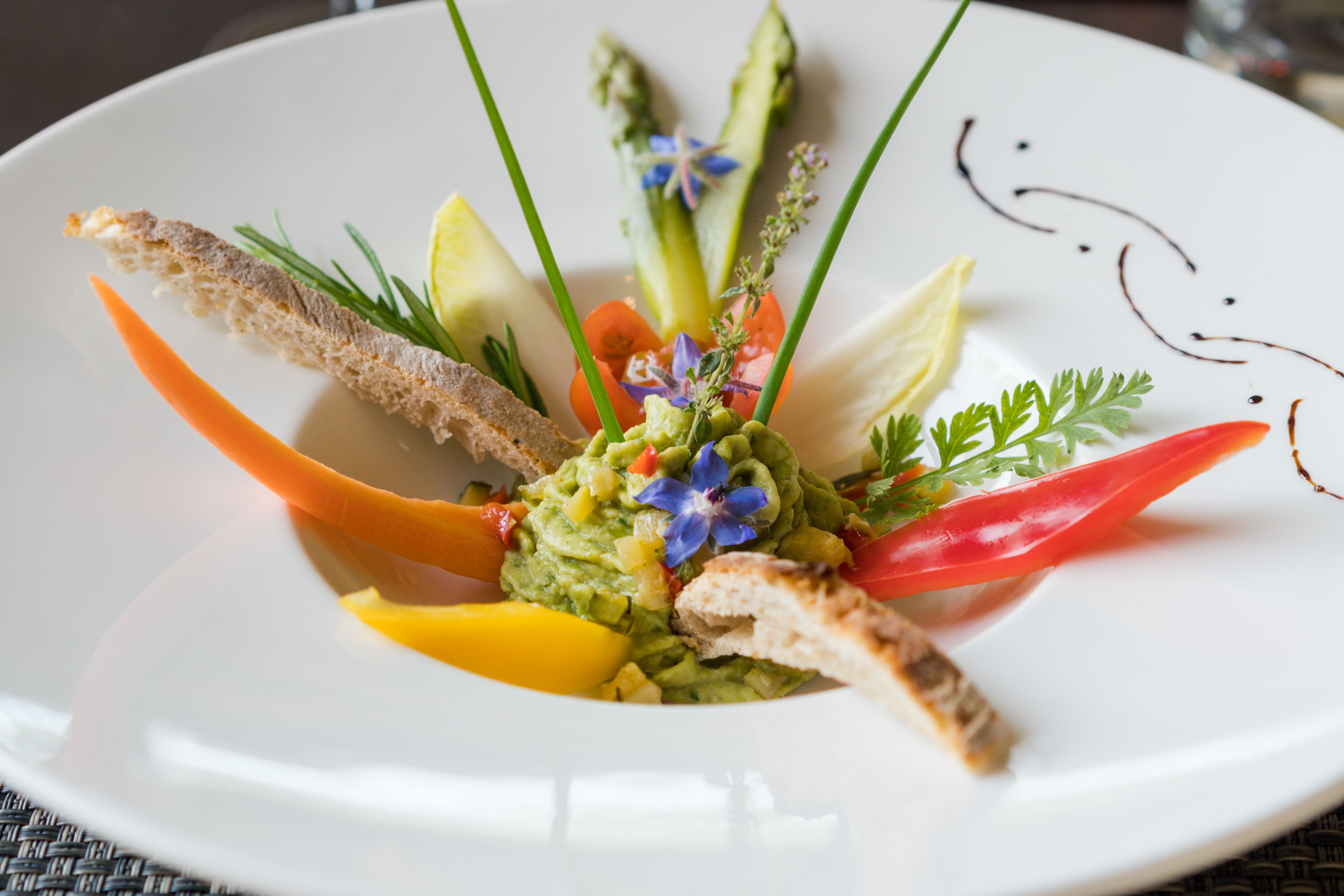 A white plate with a variety of food items including bread, vegetables, and a central avocado-based dish.