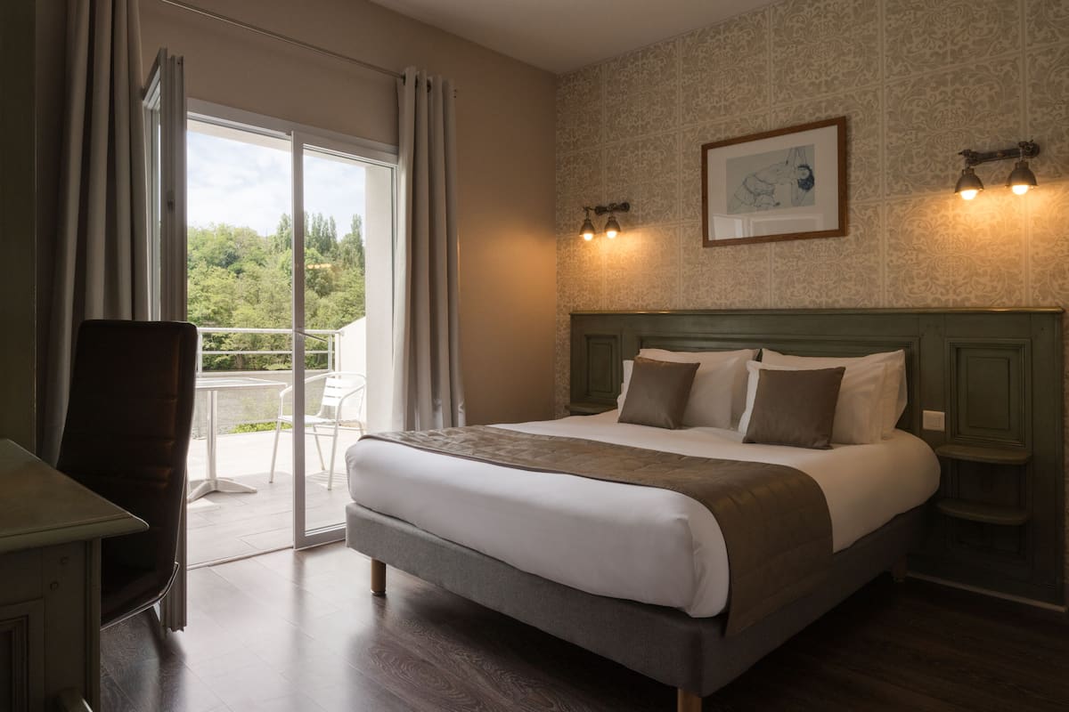 A hotel room with a large bed, a desk, and a balcony with a view of greenery.