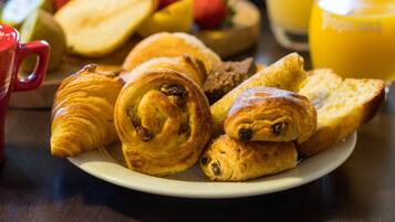 Een bord met croissants en brood, een rode mok en een glas sinaasappelsap op een tafel.