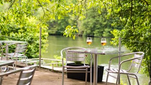 A table with two chairs and two glasses of wine, set against a backdrop of a lake and greenery. - Hotel du Lac Foix (Foix)