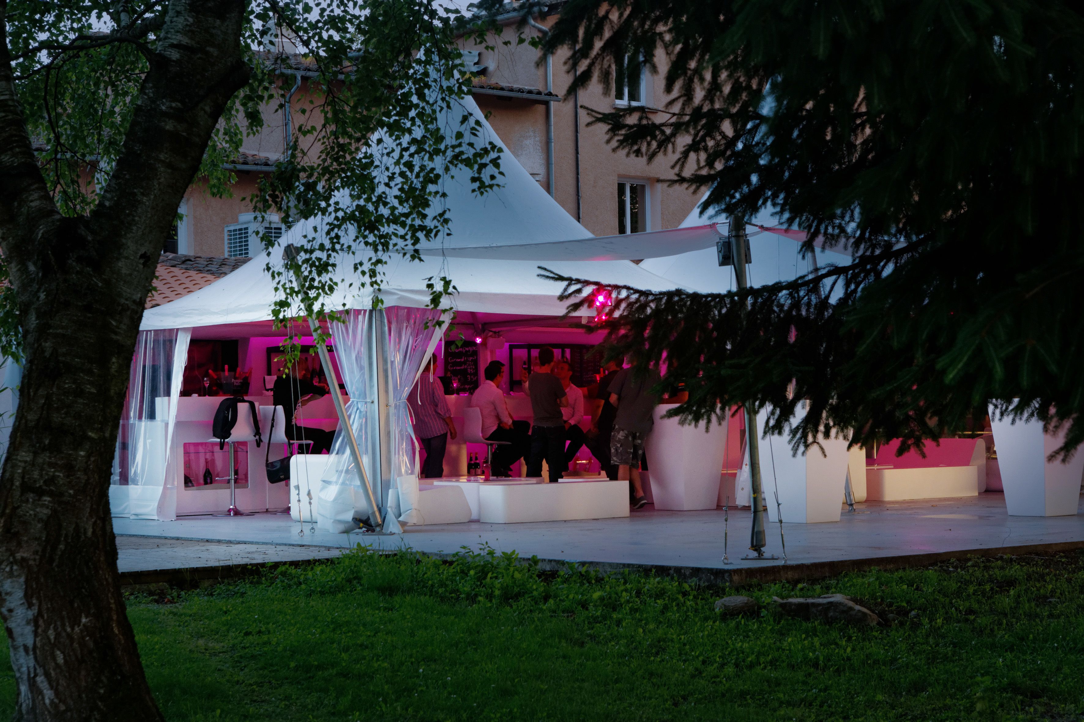 An outdoor event space with a white tent, seating areas, and a bar area.