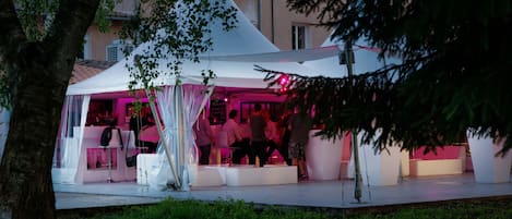 An outdoor event space with a white tent, seating areas, and a bar area.