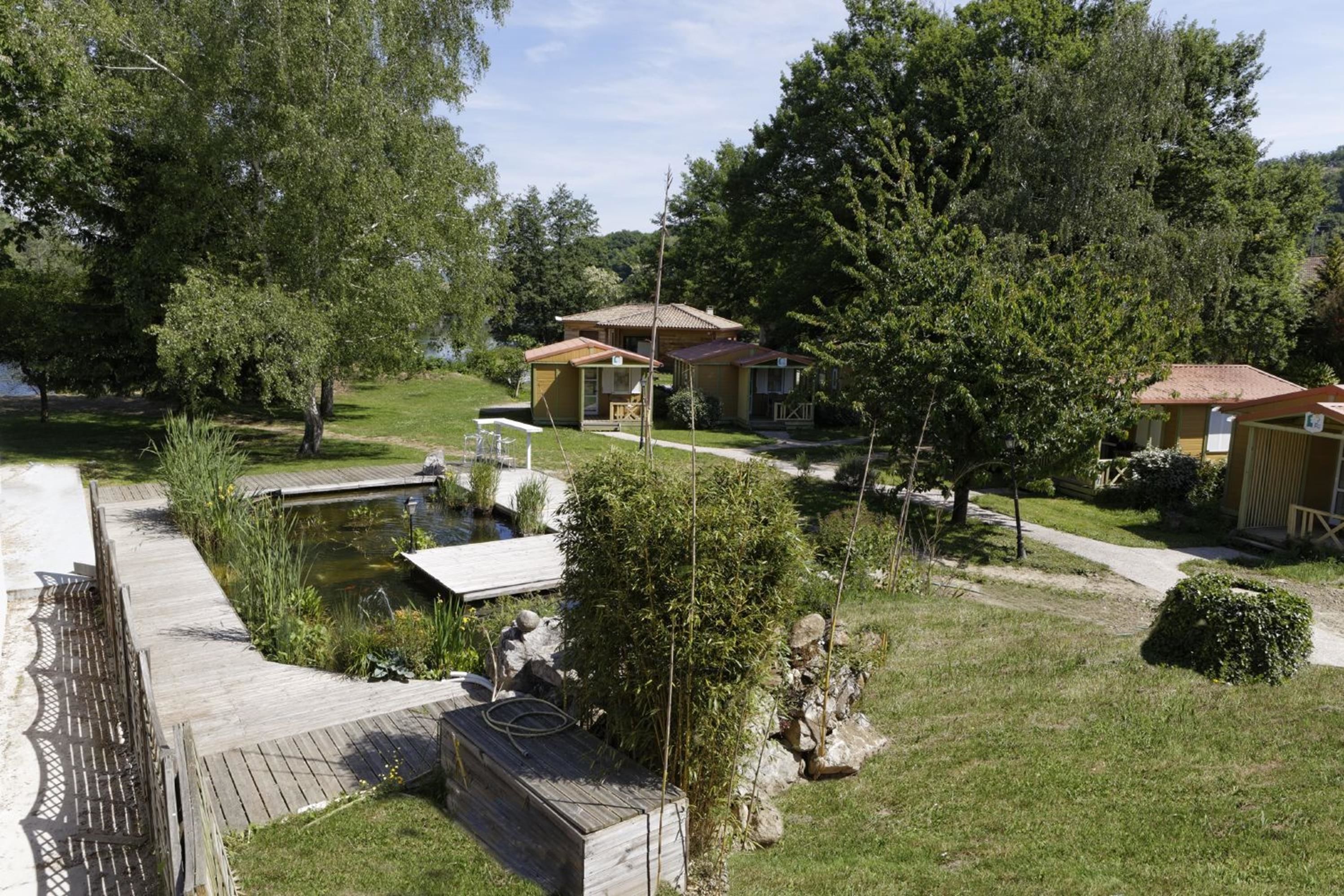 A residential area with two houses, a wooden deck, a small pond, and a pathway.