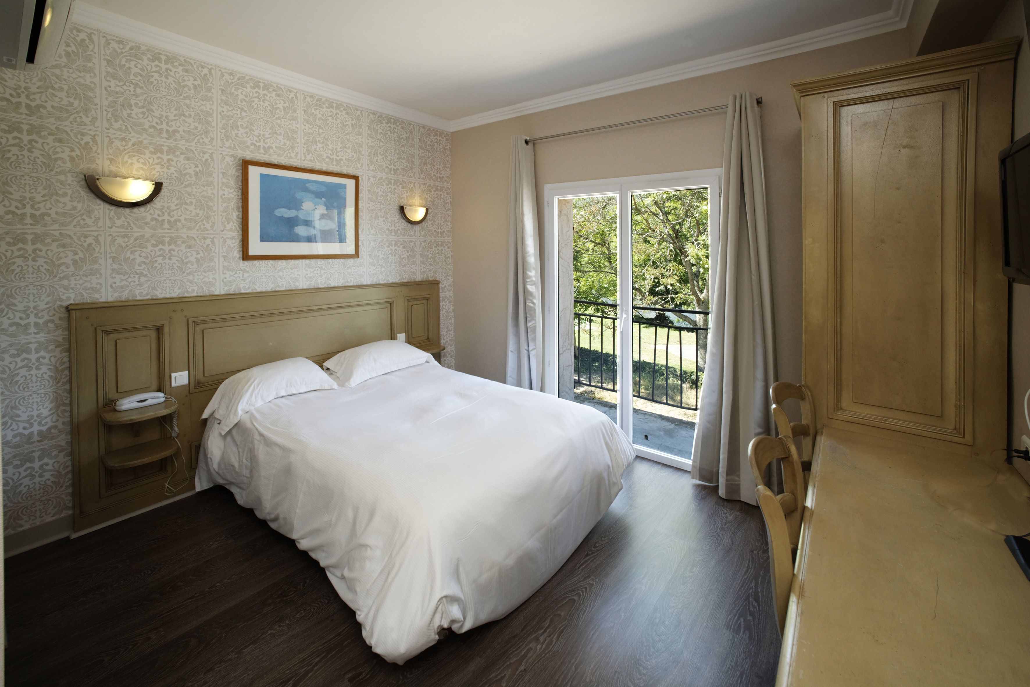 A bedroom with a large bed, a bedside table, a nightstand, a TV, and a sliding glass door leading to a balcony.