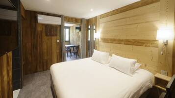 A bedroom with a wooden headboard, a bed with white linens, a bedside table with a lamp, and a view of a dining area through an open door.