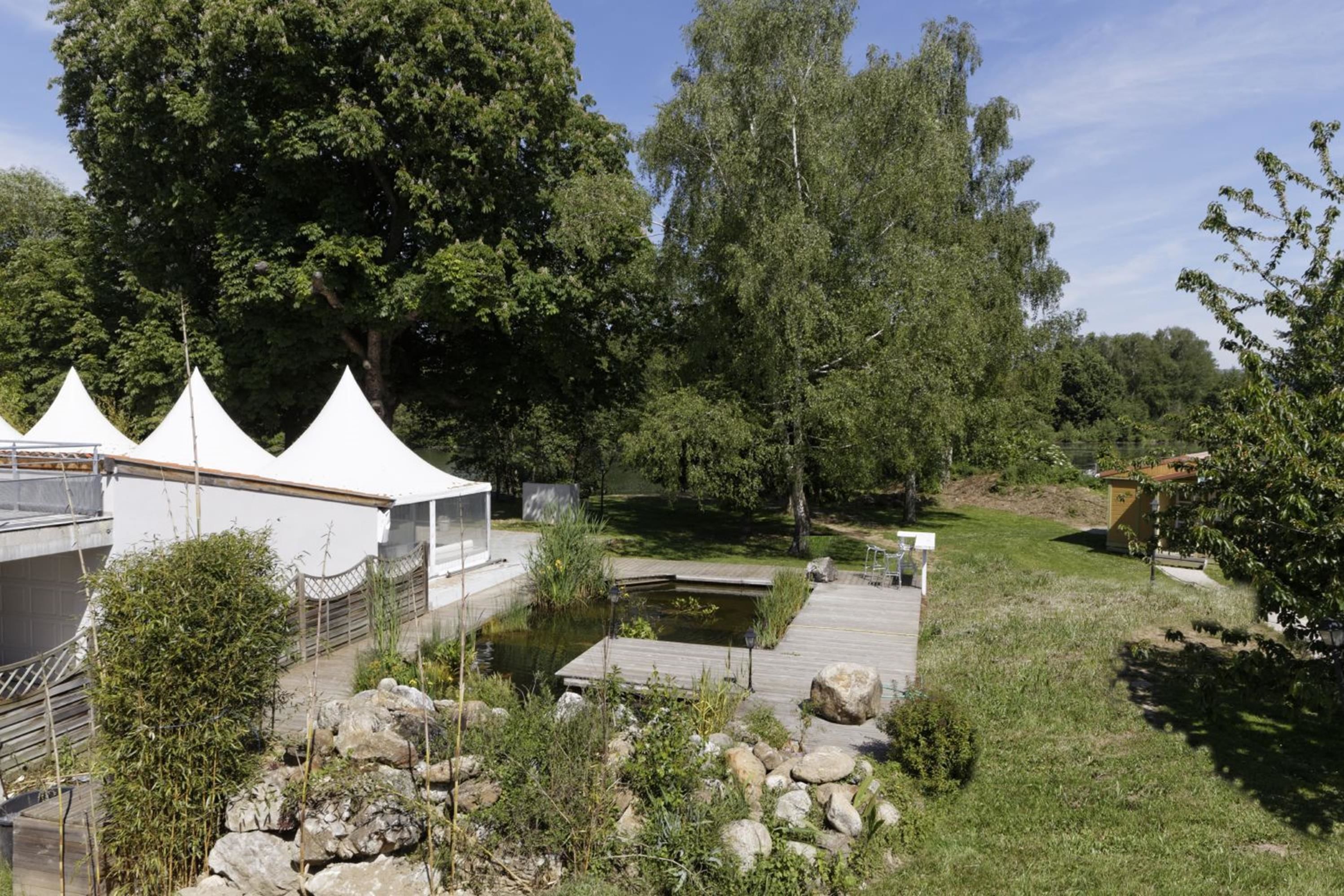 A serene outdoor setting with a wooden dock, a small pond, and white tents.