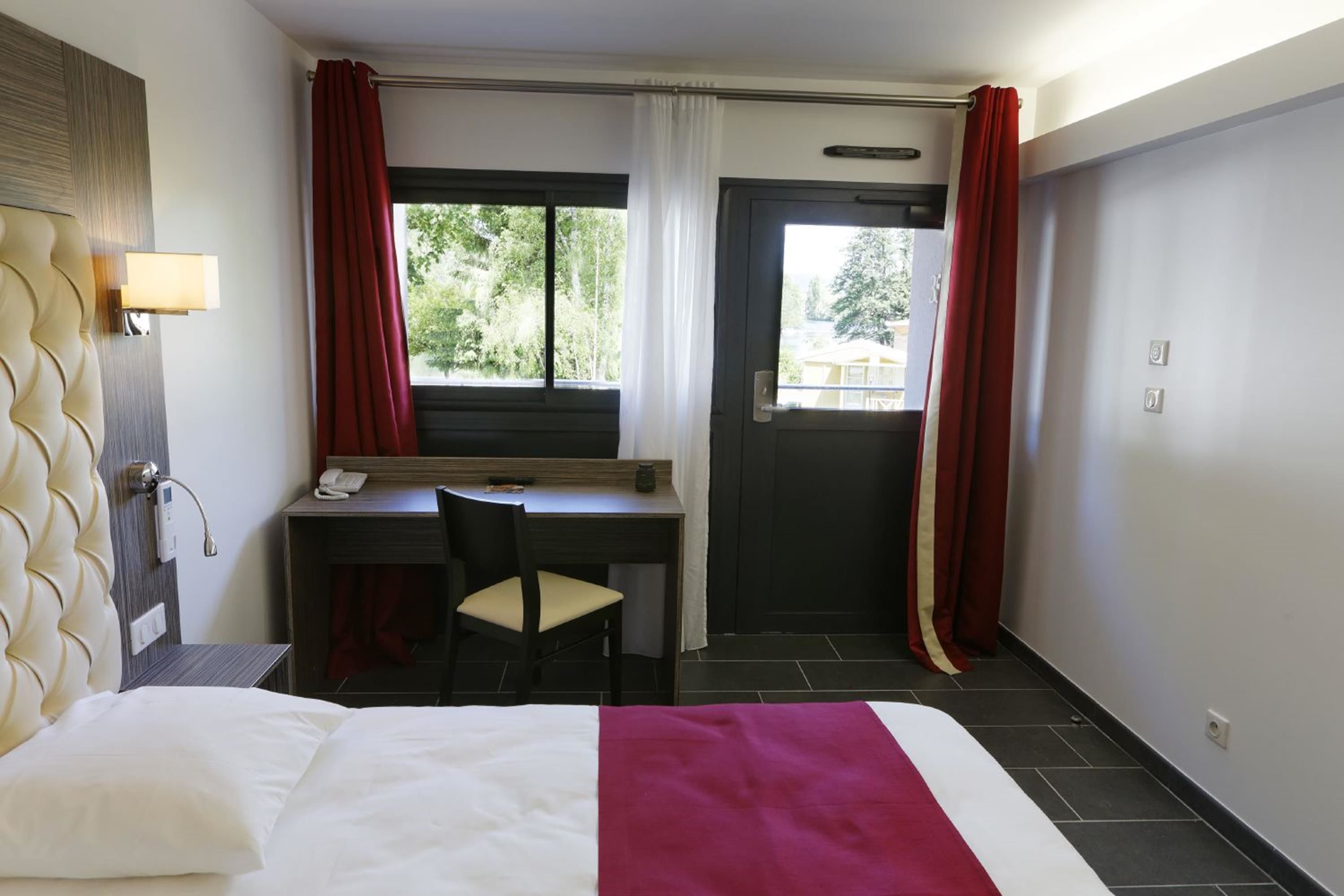 Habitación de hotel con cama, escritorio y silla, teléfono y ventana con cortinas.
